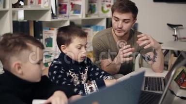 年轻迷人的男<strong>程序员</strong>老师正在向他的两个小家伙解释一些关于技术和计算机的事情